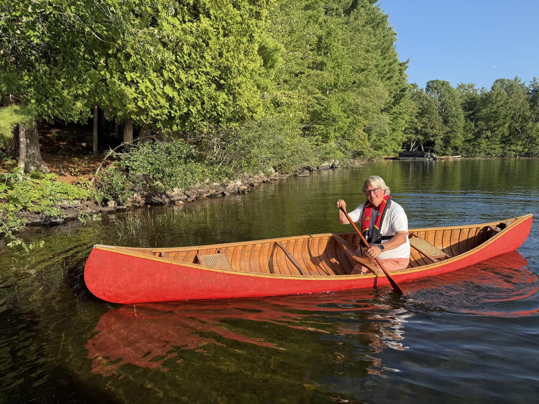 Guy Burry paddling his red canoe along a treed Muskoka shoreline